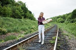 ritratto di una bella ragazza bionda in camicia scozzese che cammina sulla ferrovia con la mappa nelle sue mani. foto