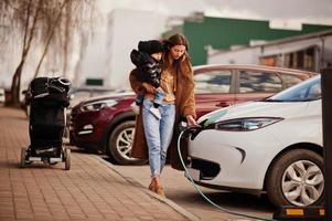 giovane madre con bambino che carica l'auto elettrica presso la stazione di servizio elettrica. foto