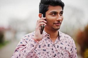 studente uomo indiano in maglietta posata all'aperto e parlando al telefono. foto