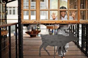 donna afroamericana in tuta e berretto poste in terrazza all'aperto con decorazioni natalizie ghirlanda e cervi. foto