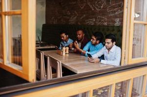 un gruppo di quattro uomini del sud asiatico poste alla riunione di lavoro nella caffetteria. gli indiani lavorano insieme usando vari gadget, conversando. foto