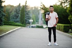 uomo alla moda con barba indiana su t-shirt rosa con giacca di pelle nera sulla spalla. modello indiano che cammina alla città di sera. foto