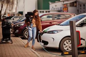 giovane madre con bambino che carica l'auto elettrica presso la stazione di servizio elettrica. foto