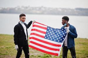 due adolescenti africani amici con bandiera americana al parco che indossano maschere mediche proteggono da infezioni e malattie quarantena del virus del coronavirus. foto