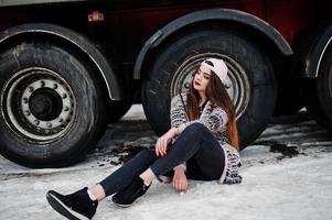 bruna ragazza casual elegante in berretto seduto contro le ruote del camion. foto