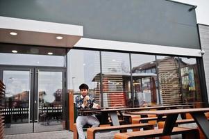 l'uomo indiano alla moda attraente e bello indossa la camicia mangia hamburger e patatine fritte sulla terrazza del moderno lounge cafe durante la sua pausa di lavoro. foto