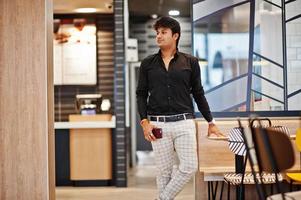 elegante uomo indiano posato al fast food cafe con il telefono cellulare a portata di mano. foto