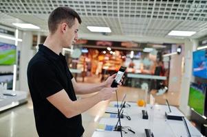 venditore uomo consulente professionale di telefonia mobile in negozio di tecnologia o negozio tenere il nuovo smartphone a portata di mano e fare selfie con la fotocamera. foto