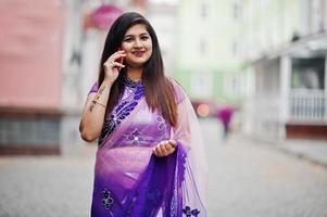 ragazza indiana indù al tradizionale saree viola posato in strada e parlando al telefono. foto