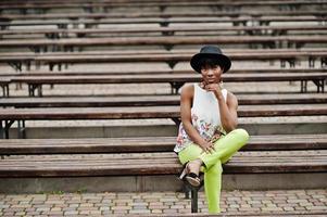 incredibile donna modello afroamericano in pantaloni verdi e cappello nero poste in panchina. foto