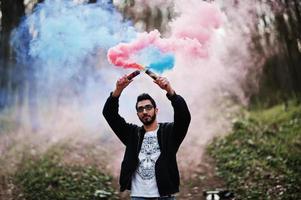 l'uomo arabo di street style con gli occhiali tiene il bagliore della mano con una bomba fumogena rossa e blu. foto