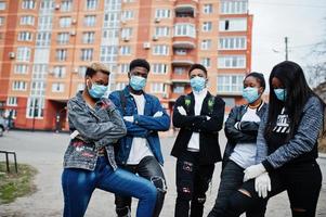 gruppo di adolescenti africani amici contro una strada vuota con edificio che indossa maschere mediche proteggere da infezioni e malattie quarantena del virus del coronavirus. foto