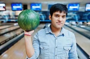 uomo asiatico alla moda in camicia di jeans in piedi alla pista da bowling con palla a portata di mano. foto