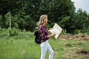 ritratto di una bella ragazza bionda in camicia scozzese che cammina con una mappa in campagna. foto