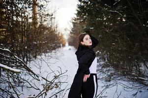 modello bruna alla moda con gambe lunghe in lungo mantello nero posato all'aperto durante la giornata invernale. foto