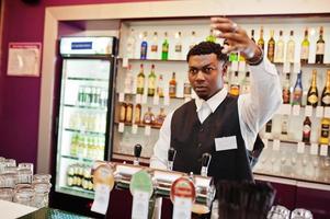 barista afroamericano al bar che versa dal rubinetto birra fresca nel bicchiere del pub. foto