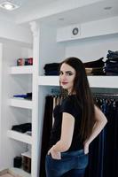bruna splendida ragazza nella boutique del negozio di abbigliamento in abiti casual, camicia nera e jeans. foto
