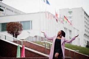 giovane ed elegante bella donna afroamericana in strada, indossando un cappotto di moda, contro le bandiere di diversi paesi del mondo. foto