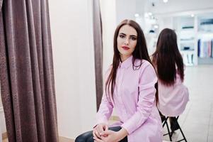 bruna splendida ragazza nella boutique del negozio di abbigliamento in abiti casual e camicetta rosa contro lo specchio. foto