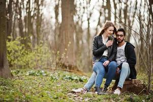 storia d'amore di una bella coppia multirazziale nella foresta primaverile. sono seduti sul ceppo. foto