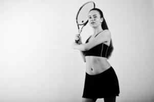 ritratto in bianco e nero di bella giovane donna giocatore in abiti sportivi che tiene la racchetta da tennis mentre in piedi su sfondo bianco. foto