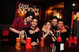 gruppo di amici indiani che si divertono e riposano al night club, bevendo cocktail e fumando narghilè. foto