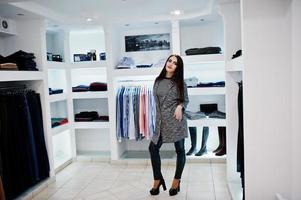 bruna splendida ragazza nella boutique del negozio di abbigliamento in abiti casual e cappotto grigio. foto