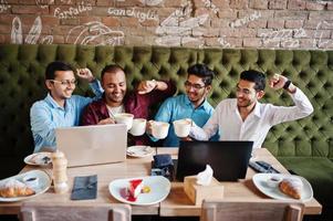 un gruppo di quattro uomini del sud asiatico poste alla riunione di lavoro nella caffetteria. gli indiani lavorano insieme con i laptop usando vari gadget, conversano e bevono caffè. foto