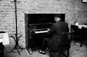 parte posteriore di un uomo afroamericano forte e potente in abito nero suona il pianoforte. foto