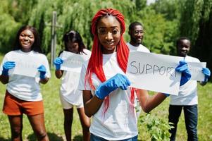 un gruppo di volontari africani felici tiene una lavagna vuota con un cartello di supporto nel parco. concetto di volontariato, carità, persone ed ecologia in africa. foto