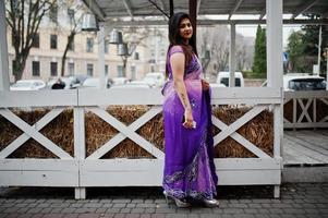 ragazza indù indiana al tradizionale saree viola poste in strada contro la terrazza in legno. foto