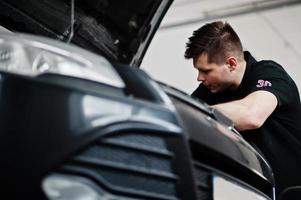 tema riparazione e manutenzione auto. meccanico in uniforme che lavora in servizio auto, controllando il motore. foto