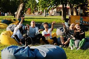 giovane gruppo multietnico di persone che guardano film a poof e lanciano popcorn nel cinema all'aperto. foto