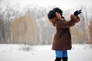 capelli ricci donna afroamericana indossare su cappotto di pelle di pecora e guanti poste al giorno d'inverno vomita neve. foto