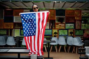 elegante donna afroamericana in occhiali da sole poste all'aperto con bandiera usa. foto