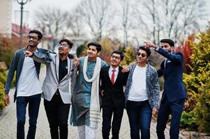 gruppo di sei uomini indiani del sud asiatico in abiti tradizionali, casual e da lavoro che camminano e mostrano le dita a qualcosa. foto