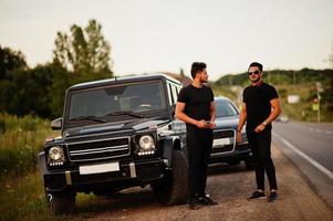 due fratelli asiatici indossano un uomo tutto nero in posa vicino alle auto suv. foto