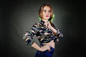 bella ragazza bruna indossare camicia militare e jeans, in posa in studio su sfondo grigio. ritratto del modello in studio. foto