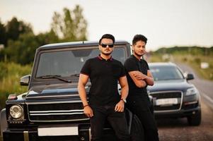 due fratelli asiatici indossano un uomo tutto nero in posa vicino alle auto suv. foto