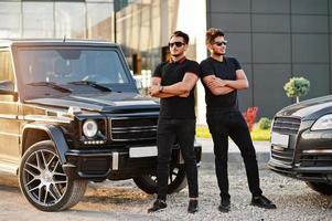 due fratelli asiatici indossano un uomo tutto nero in posa vicino alle auto suv. foto