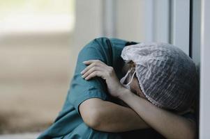 stanco depresso donna asiatica scrub infermiera indossa maschera facciale uniforme blu siede sul pavimento dell'ospedale, giovane donna medico stressato dal duro lavoro foto