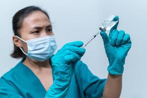 medico asiatico con siringa e vaccino per proteggere il virus covid-19 su sfondo bianco foto