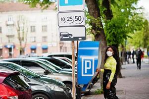 donna afroamericana in posa con maschera facciale per proteggere da infezioni da batteri, virus ed epidemie, utilizzando il terminale della stazione di pagamento del parcheggio. foto