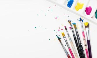 pennelli artistici e tavolozza con schizzi di vernice colorata su carta tela bianca. copia spazio foto