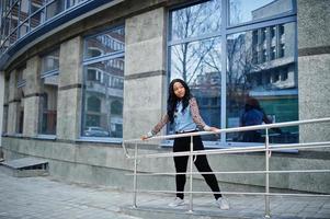 hipster ragazza afroamericana che indossa una camicia di jeans con maniche di leopardo in posa in strada contro un moderno edificio per uffici con finestre blu. foto