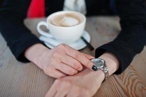 foto ravvicinata di una ragazza seduta al bar con una tazza di cappuccino e guardando i suoi orologi a portata di mano.