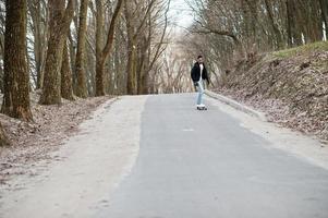 uomo arabo in stile street con occhiali da vista con longboard longboard lungo la strada. foto