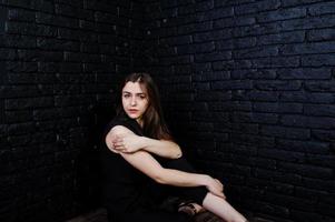 ritratto di una bella ragazza bruna in tuta nera seduta e in posa in studio. foto