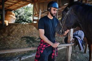 l'uomo arabo con barba alta indossa l'elmo nero con cavallo arabo. foto