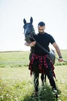 l'uomo arabo con barba alta indossa in nero con cavallo arabo. foto